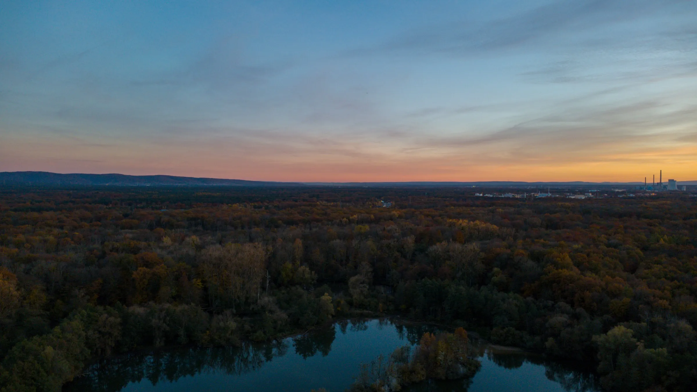 Abendliche Luftaufnahme über dem Bulau-Wald mit dem Erlensee im Vordergrund